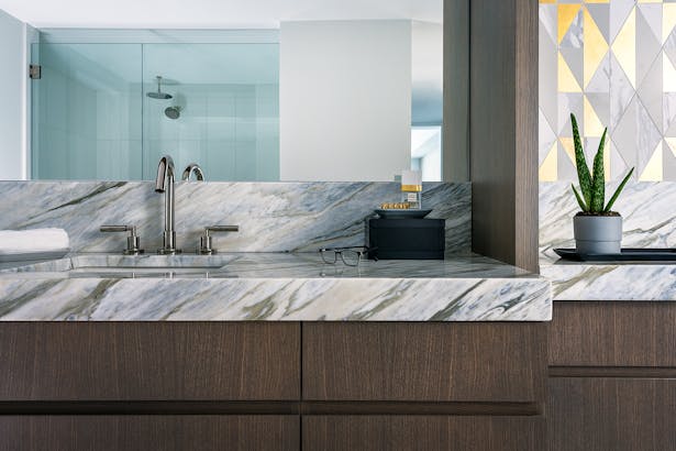 The brass accent tiles pull from the subtle gold tones in the calacatta bluette marble stone counters, which match the floors throughout the master bathroom.