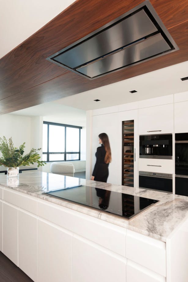 Walnut ceiling panels house a flush-mounted exhaust over the island cooktop, and extend out into the dining room. Wall appliances were confined to the opposite wall so they would be out of view as one approaches the kitchen from the main living space.