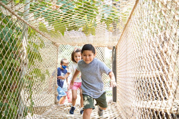 Kids running through The Treehouse's rope tunnel above the exhibits below. Photo credit: Artem Nazarov Photography