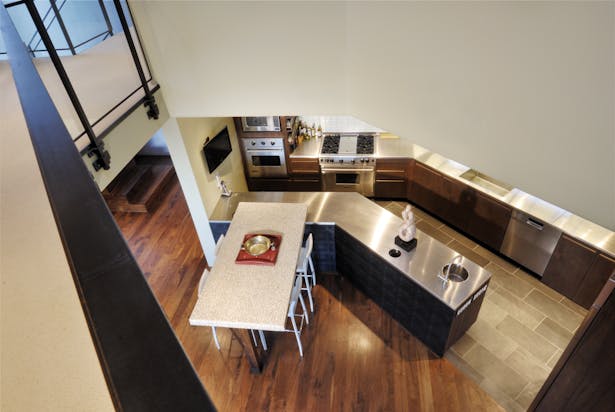 A double-height ceiling cutout and black walnut flooring connect the living area and the kitchen, which features a custom stainless-steel countertop and black slate floor. Cummins ordered the custom tabletop, which was made in China using smooth, cream-colored riverstones set in clear resin.