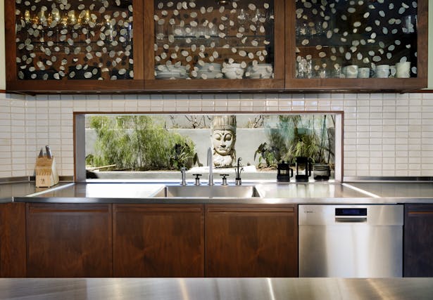 A slot window was used instead of a traditional backsplash, opening the kitchen to the view of a small side yard. The cabinet fronts were inset with Livinglass, in which Roman Coin leaves were embedded in a resin layer between two sheets of recycled glass. White crackled tile from Ann Sacks.