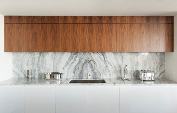 The symmetry of the kitchen's back wall is amplified by the repeating veneer and book matched quartzite backsplash, bringing an austere formality to the kitchen.
