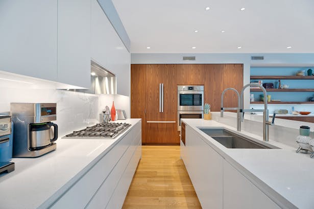 A mix of white in the kitchen - painted cabinets, soft white Caesarstone countertops, and a faux marble backsplash - are paired with custom natural walnut cabinetry to house the fridge, ovens, and pantry cabinets. Credit: Brian Bailey