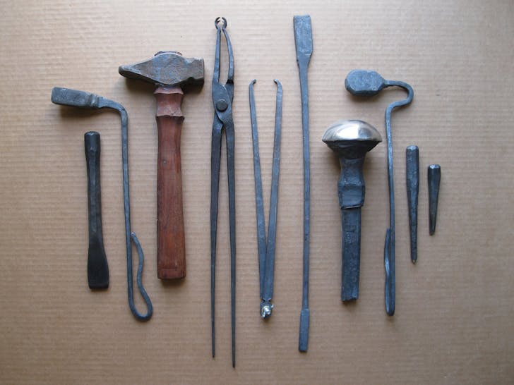 Tools made in William Bastas Toolmaking and Power Hammer classes. From Left to Right—chisel, fullering tool, hammer, tongs, caliper, hacker/snapper, mushroom stake, spoon shaped fullering tool, center punch, graver.