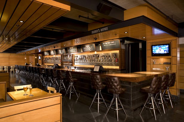 The back bar is a trophy wall that showcases each unique tap in its glory, and interior walls are then finished in wood panels in a luscious honey color with linear patterns to help create the effect of an elongated space.