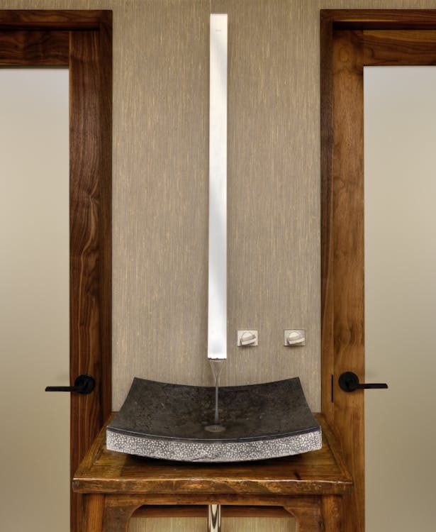The powder room is defined by a long stainless steel wall-mounted fixture that emphasizes a single antique Asian table with a granite basin.