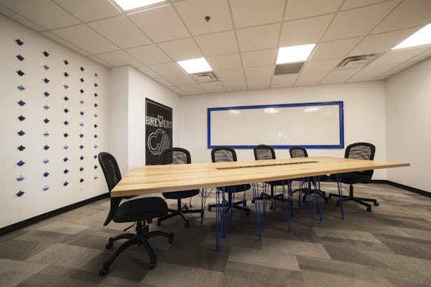 Conference room with 'brewery' theme. An array of bottle openers fills the wall as well as a custom fabricated conference table by Synecdoche. Table is built with 20 hairpin legs and white oak boards.